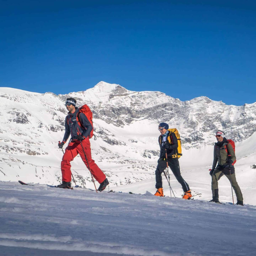 Skitourengeher auf verschneiter Alm mit Bergpanorama im Hintergrund.