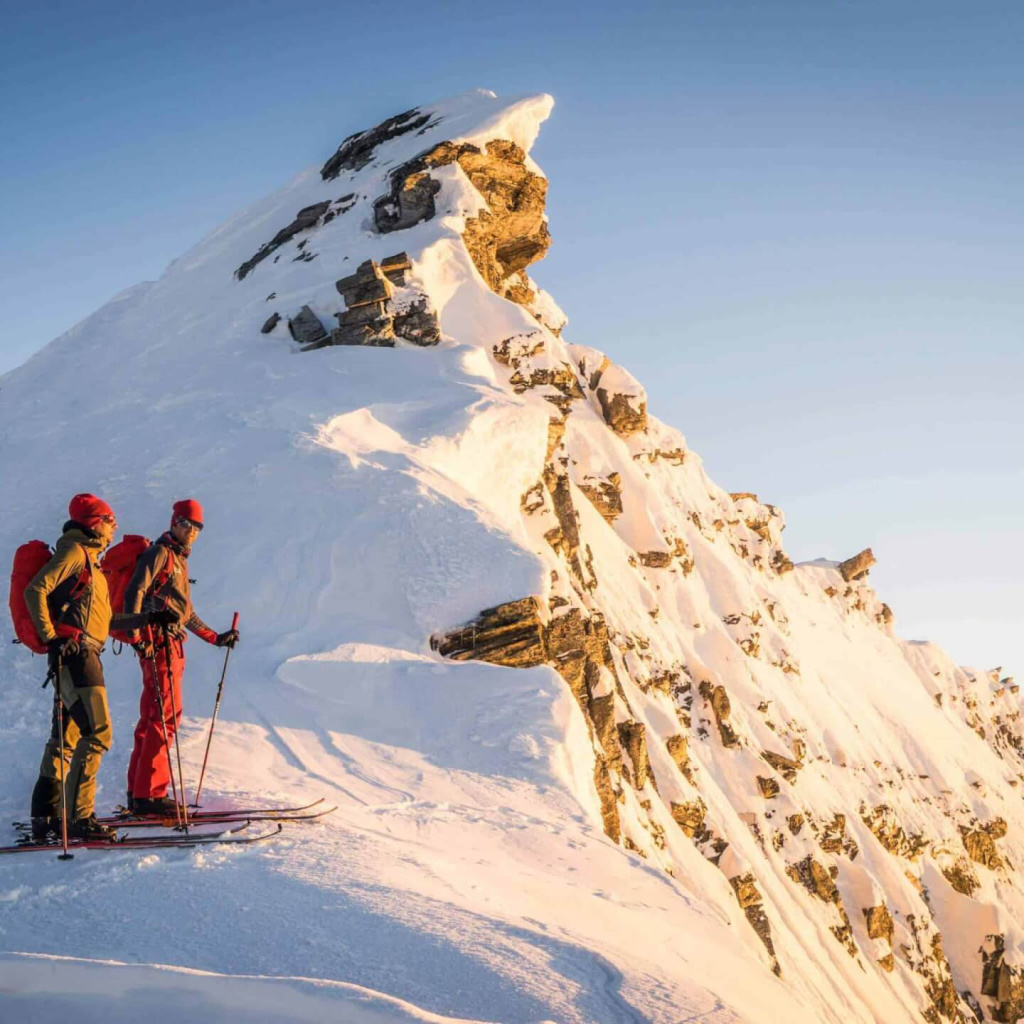 Skitourenfahrer stehen am schneebedeckten Gipfel der Alpen bei Sonnenuntergang.
