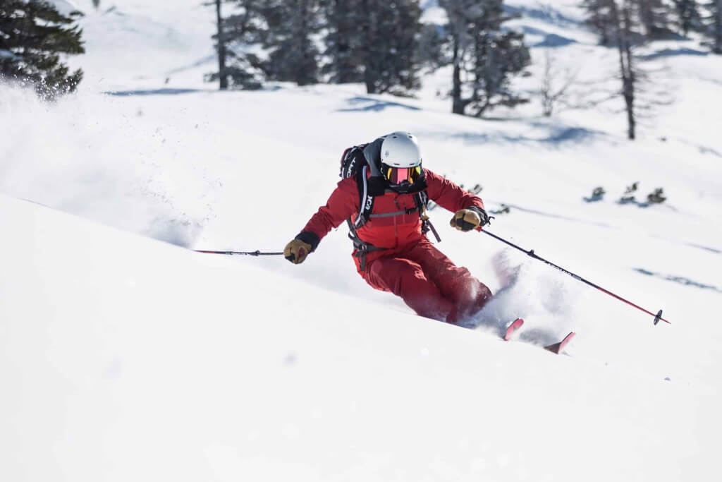Skifahrer in roter Ausrüstung fährt durch frischen Pulverschnee in den Alpen.