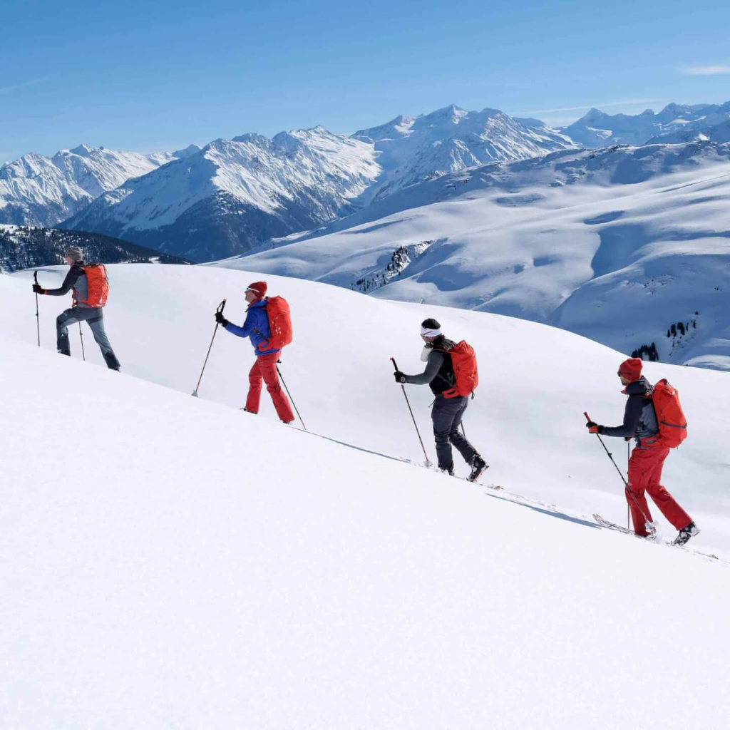 Skibergsteiger wandern durch die verschneiten Alpen unter blauem Himmel.