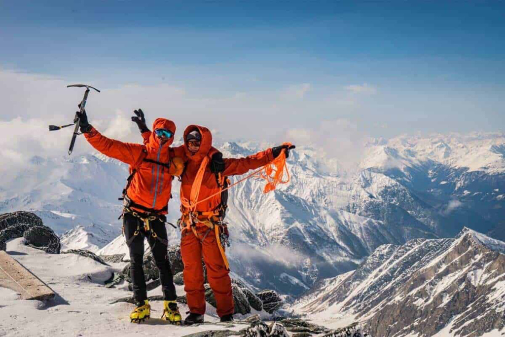Bergsteiger in orangeebene Kleidung feiern den Gipfelsieg in den verschneiten Alpen.