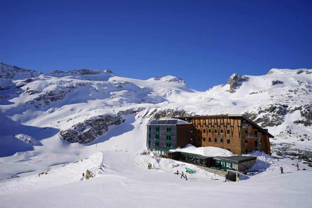 Skitourenhochcamp Rudolfshütte mit schneebedeckten Alpen im Hintergrund bei klarem Wetter.