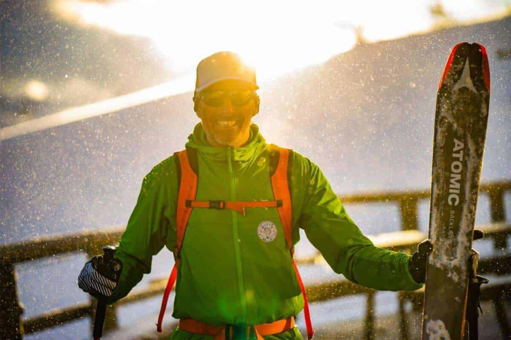 Skiführer mit Ausrüstung im Schnee vor sonnigem Alpenhorizont, bereit für Skitouren.