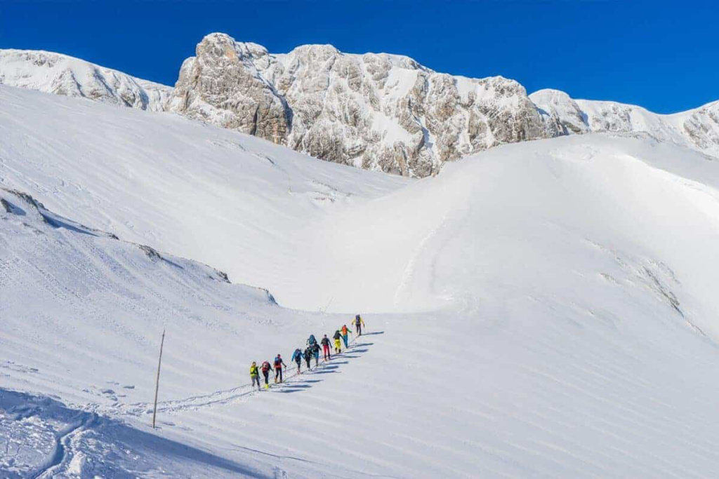 Gruppe von Skitourengehern wandert durch verschneite Alpenlandschaft bei strahlendem Sonnenschein.