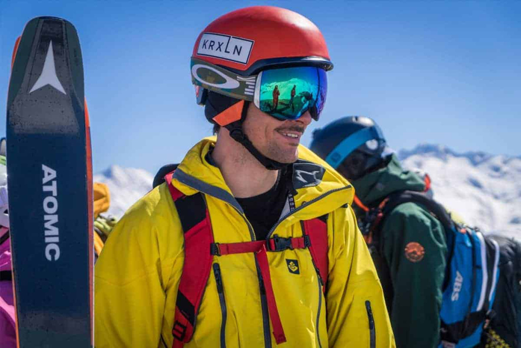 Skitourenfahrer in gelber Jacke und Helm mit Blick auf die alpine Berglandschaft.