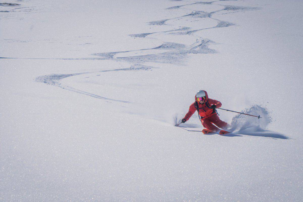 Skitourengeher in oranger Ausrüstung schwingt durch frischen Pulverschnee in den Alpen.
