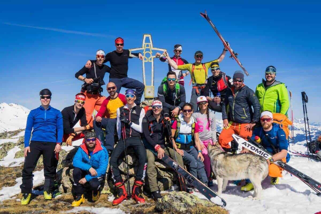 Gruppe von Skitourengehern auf einem Gipfel mit Ski und Ausblick auf die Alpen.