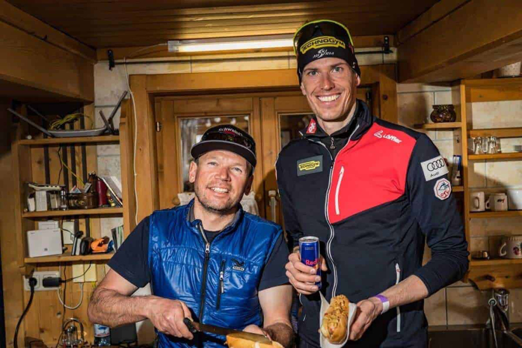 Zwei Männer in Sportkleidung bereiten sich in einer Hütte auf ein Skiabenteuer vor.