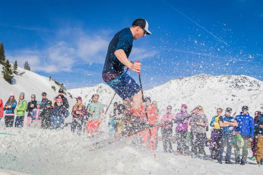 Skifahrer springt durch schneebedecktes Gelände, Zuschauer genießen das Wintererlebnis.