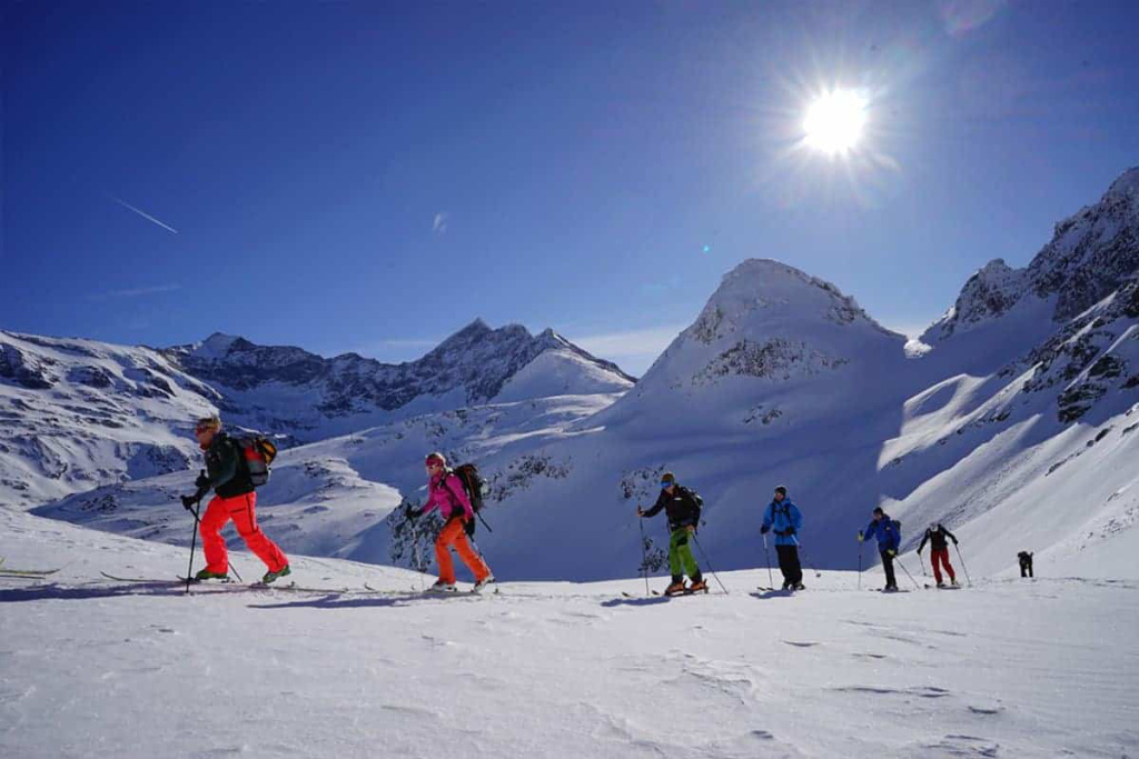 Skibergsteiger auf Tour in den Alpen, umgeben von schneebedeckten Gipfeln und Sonnenschein.