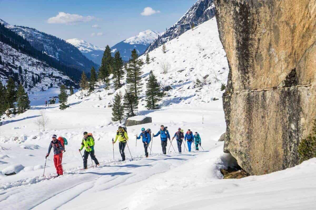 Gruppenausflug auf Skitouren durch verschneite Alpenlandschaft mit Bäumen und Bergen.
