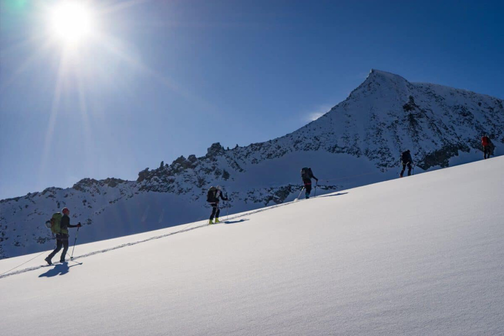 Skitourengeher am Schnee mit Berggipfel und strahlender Sonne im Hintergrund.
