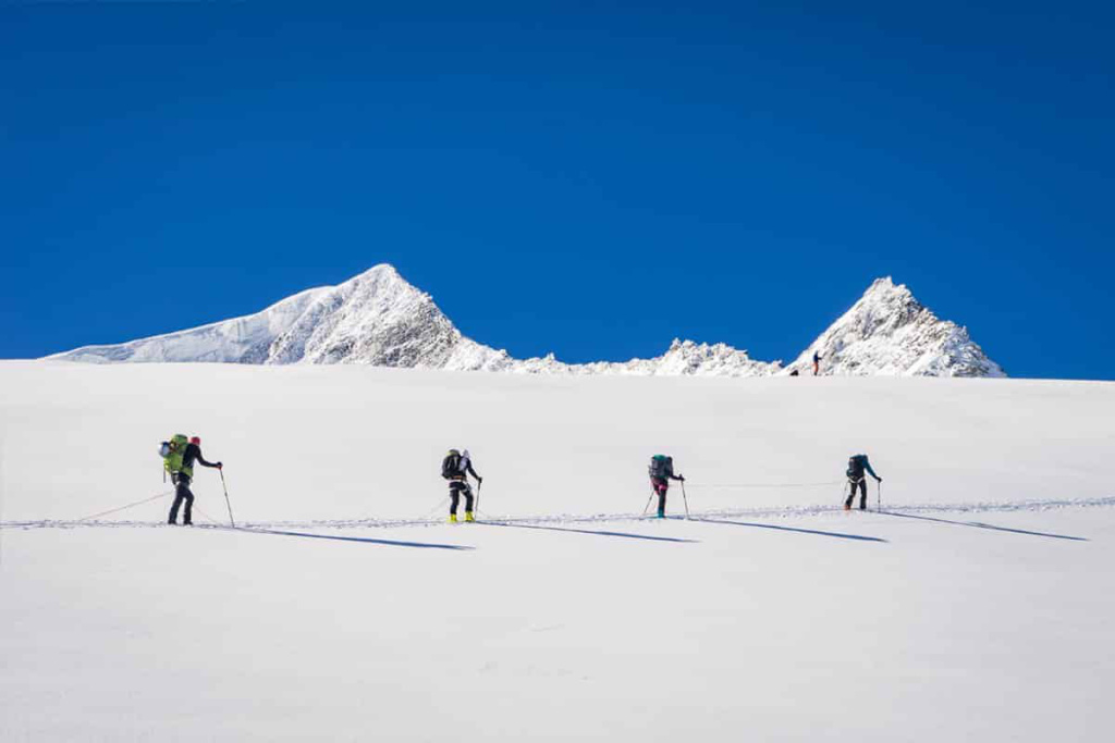 Skitouren-Gruppe wandert durch verschneite Alpenlandschaft unter blauem Himmel.